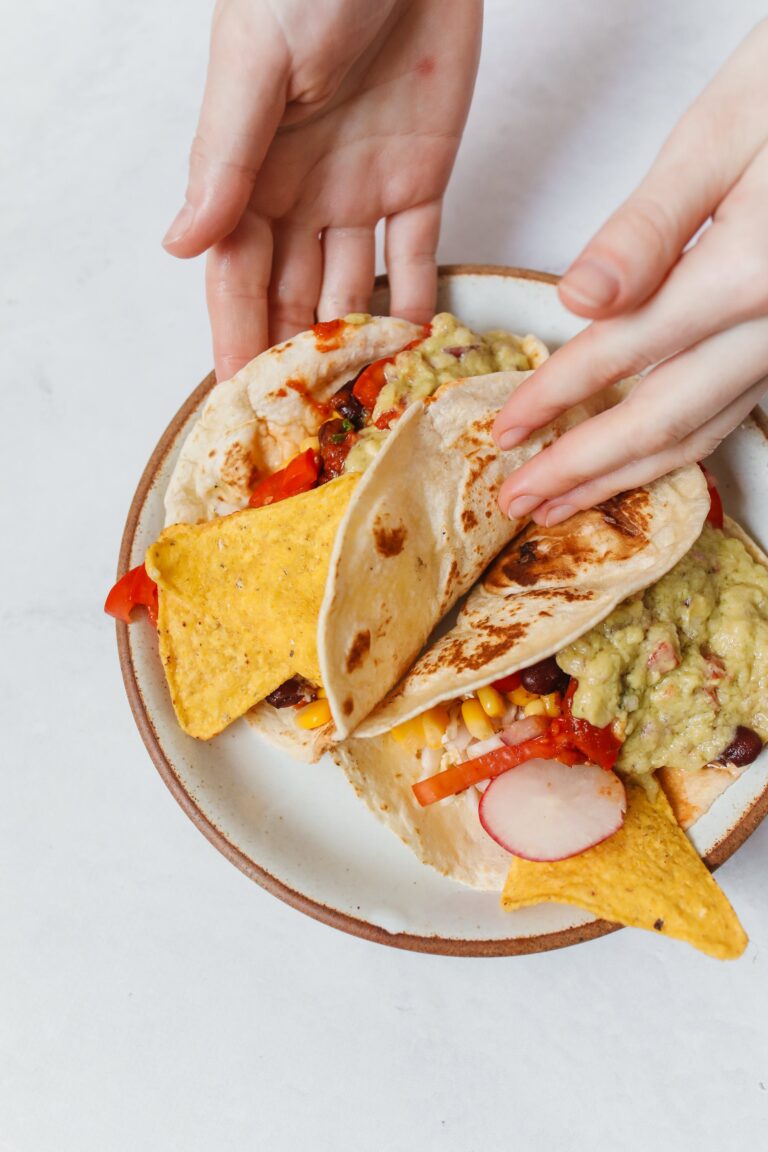 A close-up view of colorful tacos with guacamole and nachos on a plate, being held by hands.